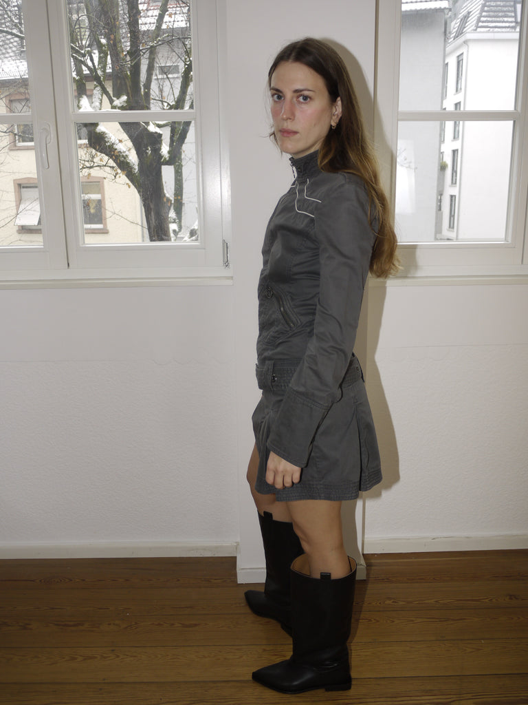 Vintage Diesel zip-up mini dress in faded black denim, utility-style jacket dress with contrast stitching and stand-up collar, Y2K grunge aesthetic, styled with black boots indoors.