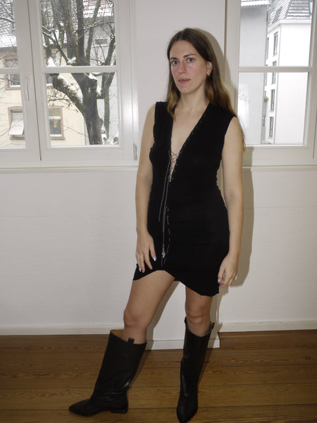 Vintage Jean Paul Gaultier-style black sleeveless dress with deep V-neck and asymmetric hemline, featuring body-hugging ruching and edgy details. Styled with black boots for a bold and feminine silhouette in true Gaultier spirit.