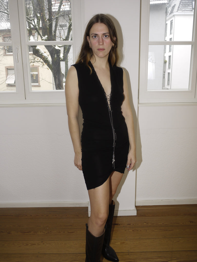 Vintage Jean Paul Gaultier-style black sleeveless dress with deep V-neck and asymmetric hemline, featuring body-hugging ruching and edgy details. Styled with black boots for a bold and feminine silhouette in true Gaultier spirit.