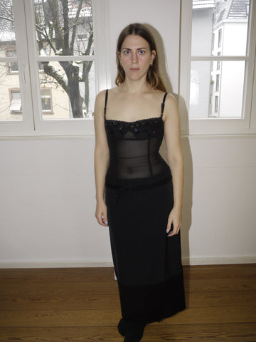 Black mesh bustier top with delicate pearl embellishments and structured cups, elegant sheer layering piece styled with long black skirt, eveningwear look modeled indoors.

