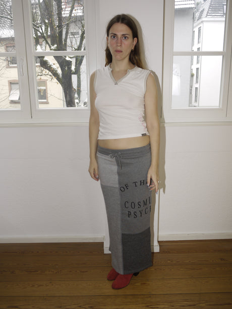 Alexander McQueen McQ grey maxi skirt with bold black text print, avant-garde streetwear vibe, Y2K-inspired silhouette, styled with sleeveless top and red boots, worn by model indoors.
