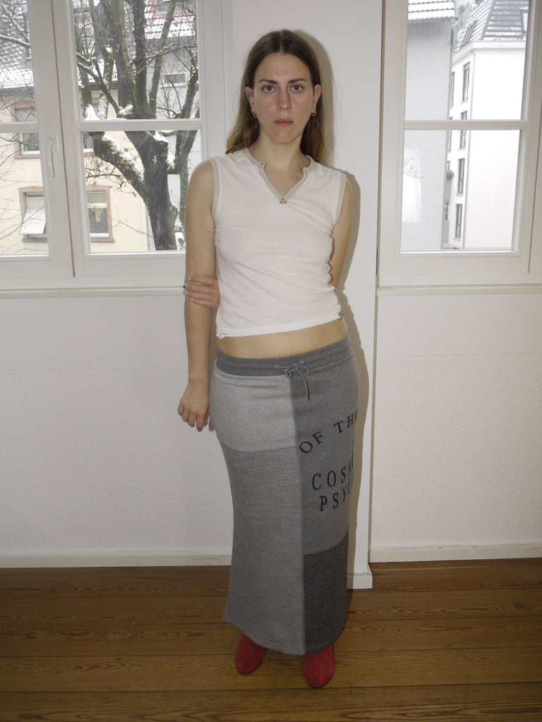 Alexander McQueen McQ grey maxi skirt with bold black text print, avant-garde streetwear vibe, Y2K-inspired silhouette, styled with sleeveless top and red boots, worn by model indoors.