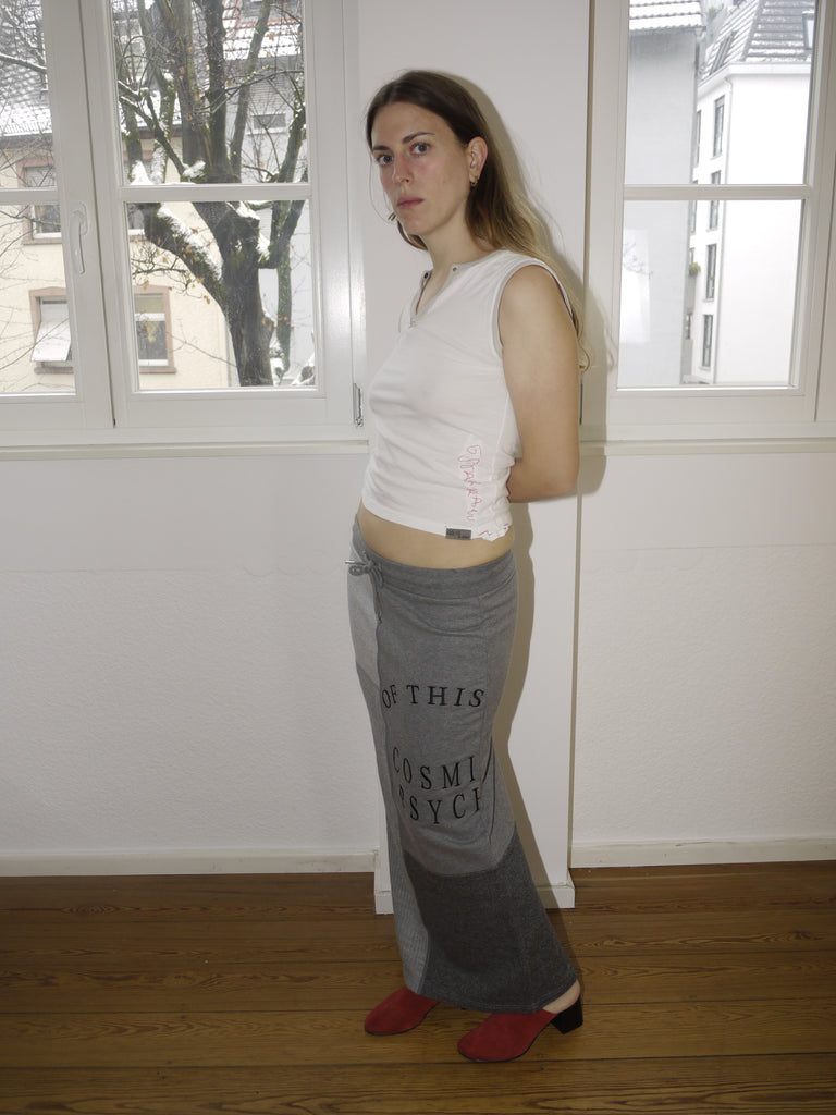 Alexander McQueen McQ grey maxi skirt with bold black text print, avant-garde streetwear vibe, Y2K-inspired silhouette, styled with sleeveless top and red boots, worn by model indoors.