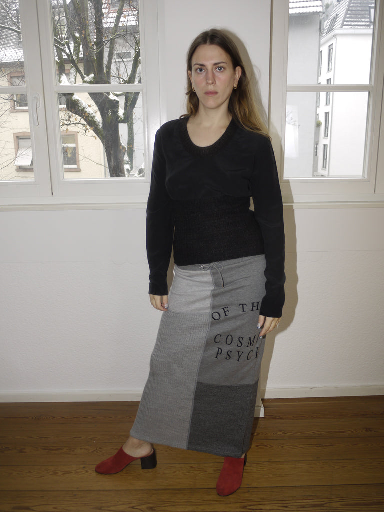 Avant-garde black long sleeve top with layered textures, inspired by Dries Van Noten’s signature deconstructed aesthetic, styled with grey Y2K print skirt, worn by model in natural light.