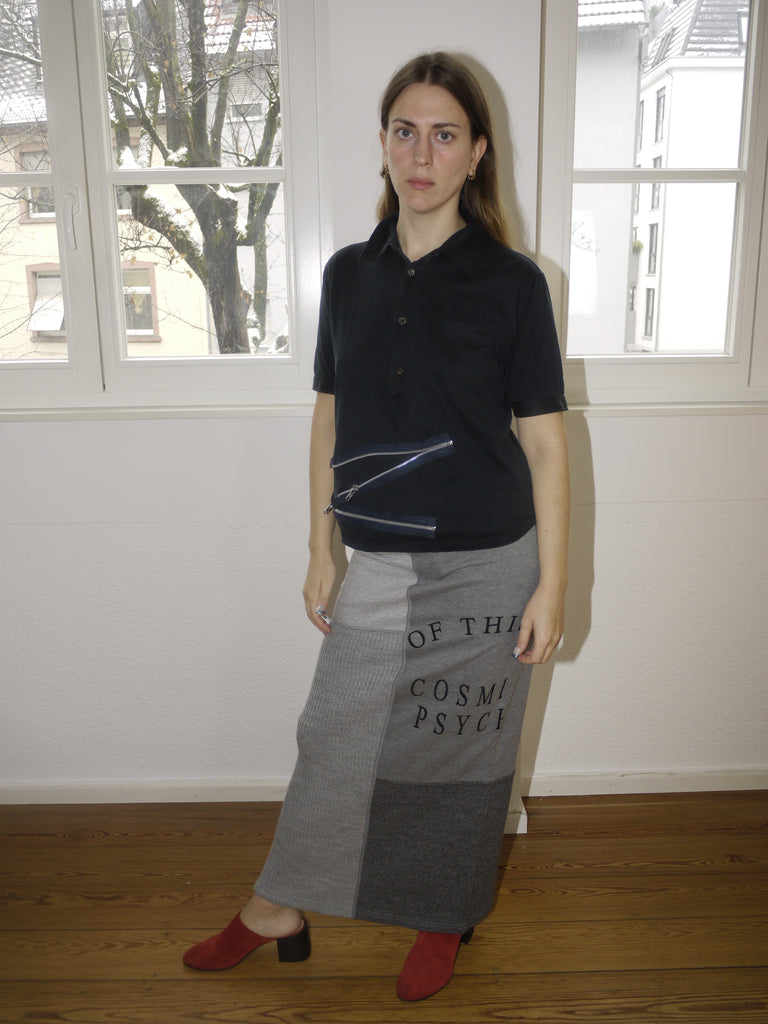 Alexander McQueen McQ grey maxi skirt with bold black text print, avant-garde streetwear vibe, Y2K-inspired silhouette, styled with sleeveless top and red boots, worn by model indoors.