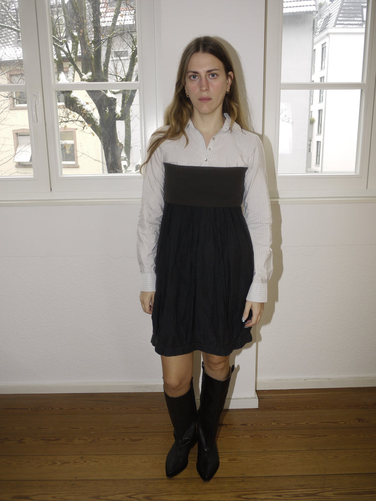 Original Cop Copine black pleated mini dress with white contrast collar and long sleeves, playful schoolgirl-inspired design, styled with black boots, modeled indoors.