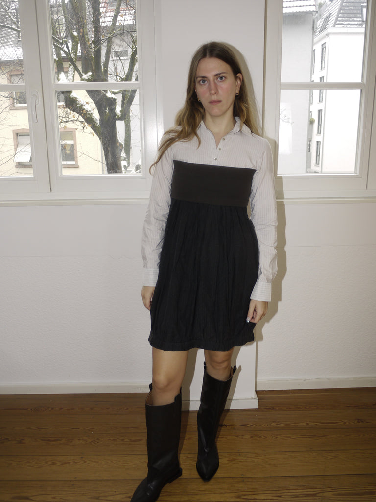 Original Cop Copine black pleated mini dress with white contrast collar and long sleeves, playful schoolgirl-inspired design, styled with black boots, modeled indoors.