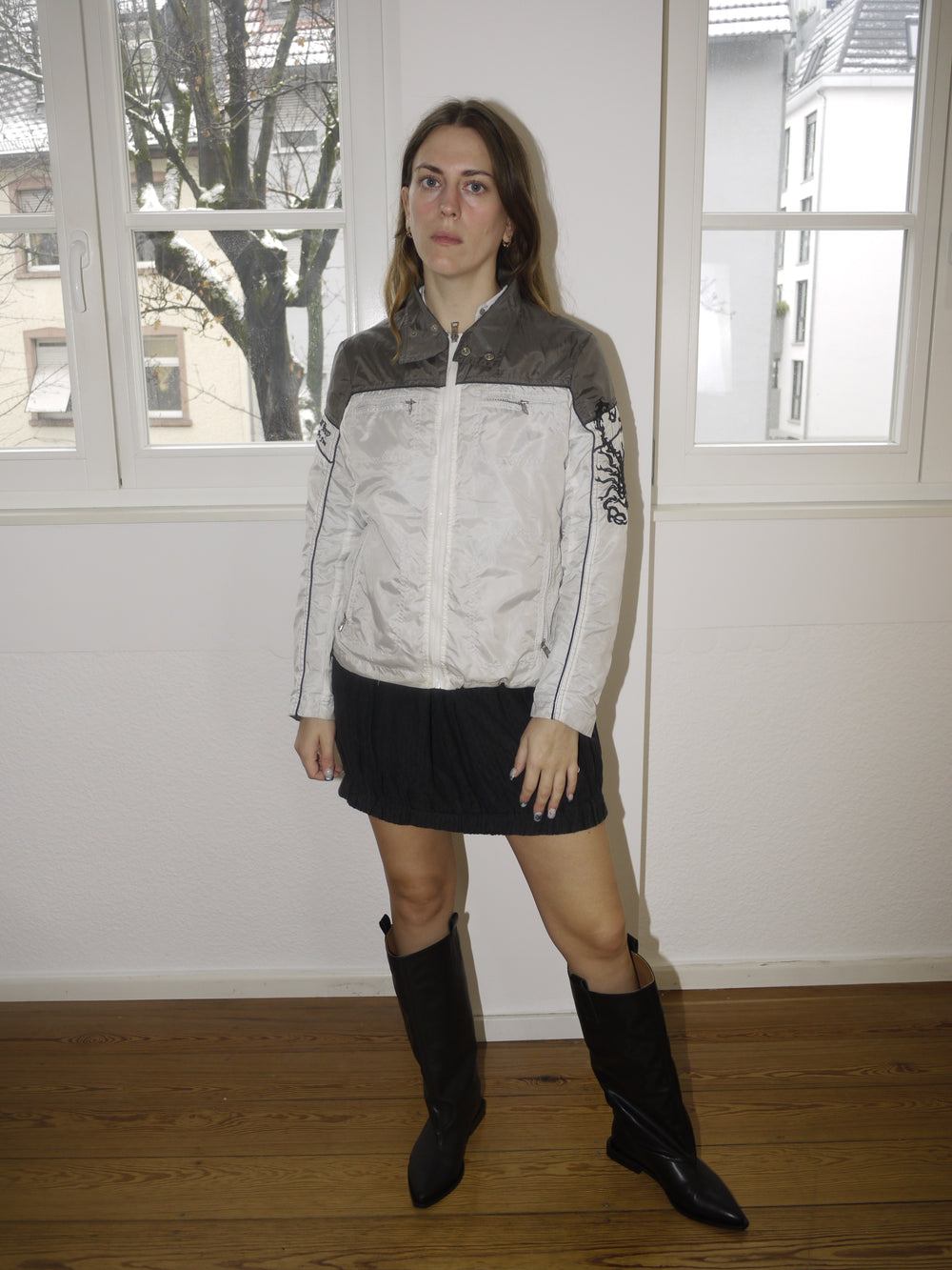 Vintage two-tone white and grey bomber jacket with embroidered scorpion motif on the sleeve, zip-up front and sporty silhouette, styled with black mini skirt and boots, modeled indoors.