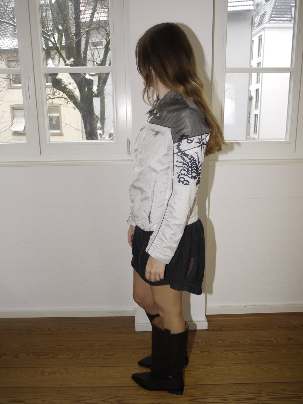 Vintage two-tone white and grey bomber jacket with embroidered scorpion motif on the sleeve, zip-up front and sporty silhouette, styled with black mini skirt and boots, modeled indoors.