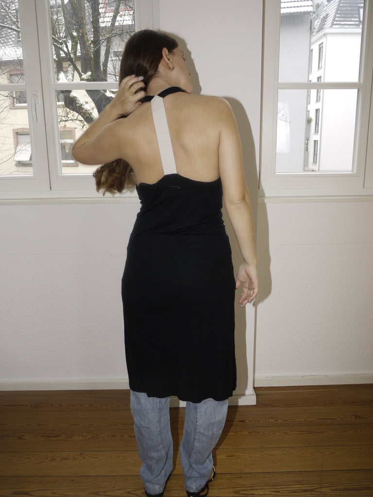 Vintage black Margiela-style halterneck dress with beige side stripe and open back, styled over jeans and modeled indoors in natural light. Draped fit with a modern, deconstructed vibe reminiscent of Maison Margiela aesthetics.