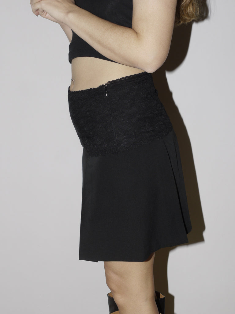 Vintage black midi skirt with low-rise fit and textured waistband detail. Styled with a knit vest and boots for a playful, eclectic look with slight Y2K and craftcore vibes.