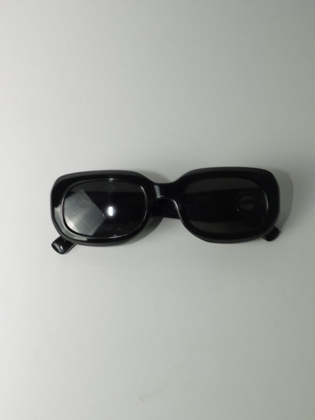 Vintage Longchamp sunglasses in glossy black with a rectangular frame and dark lenses, laid flat on a light surface.