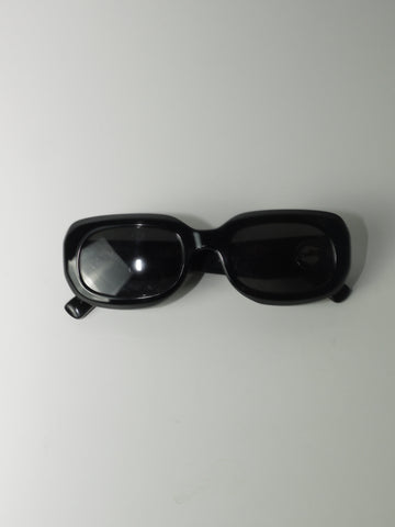 Vintage Longchamp sunglasses in glossy black with a rectangular frame and dark lenses, laid flat on a light surface.