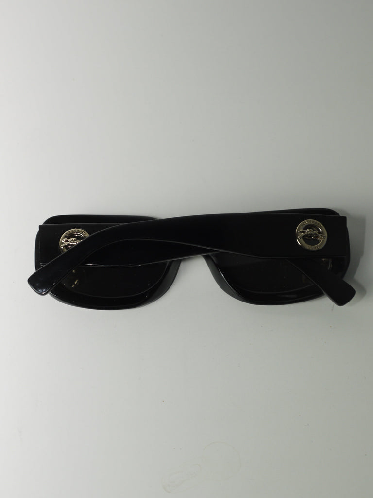 Vintage Longchamp sunglasses in glossy black with a rectangular frame and dark lenses, laid flat on a light surface.