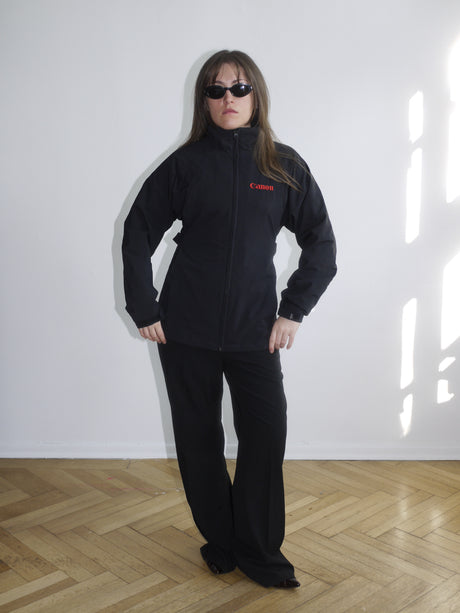 Black Canon branded zip-up jacket with red logo embroidery on the chest, worn with matching black pants. Sporty and utilitarian look with a boxy fit.