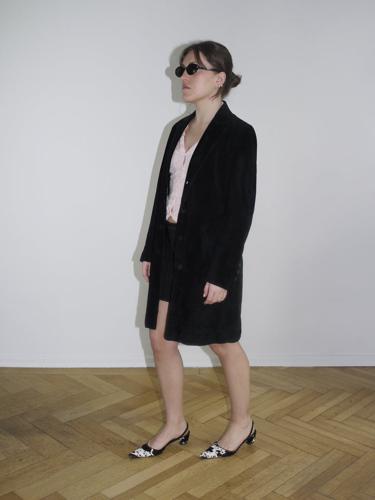 Black vintage leather coat with minimalist cut, styled with cow-print kitten heels. A sleek Margiela-inspired silhouette, perfect for spring layering.