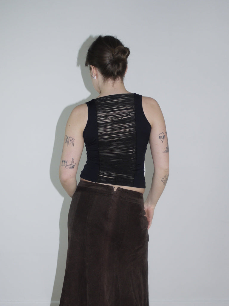 Black sleeveless backless top with long hanging fabric bands, styled with a brown flared suede maxi skirt. A Cop Copine-inspired silhouette, perfect for spring layering