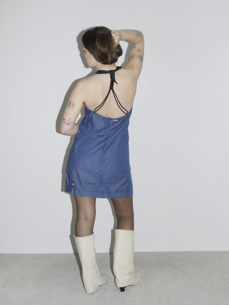 Model in a fitted dark blue halterneck mini dress by G-Star, styled with off-white knee-high boots – a sleek Y2K-inspired silhouette with utilitarian edge.
