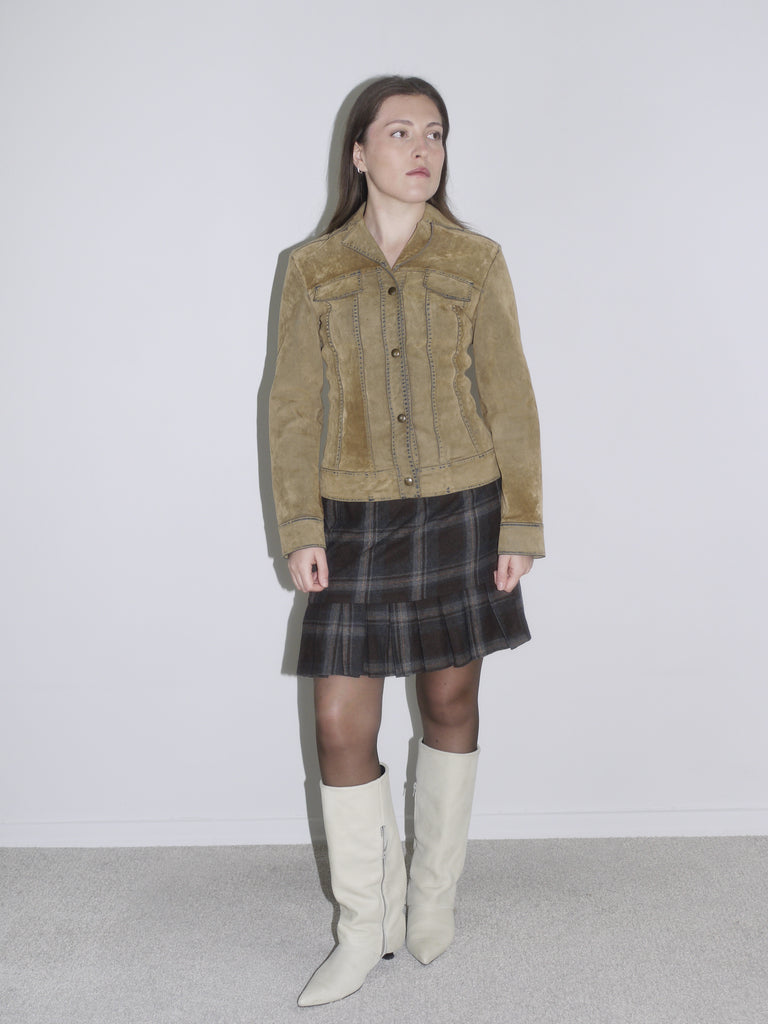 Woman wearing a structured camel suede jacket with contrast stitching, paired with a dark plaid mini skirt