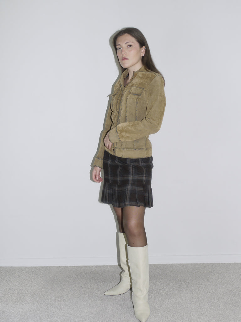 Woman wearing a structured camel suede jacket with contrast stitching, paired with a dark plaid mini skirt