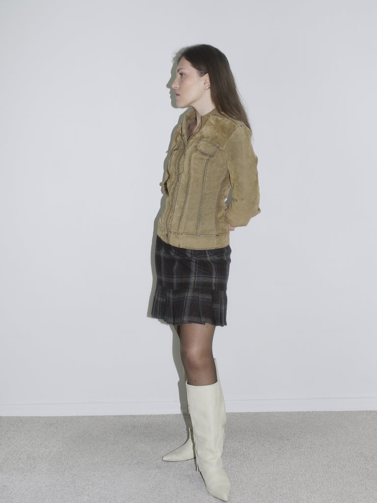 Woman wearing a structured camel suede jacket with contrast stitching, paired with a dark plaid mini skirt