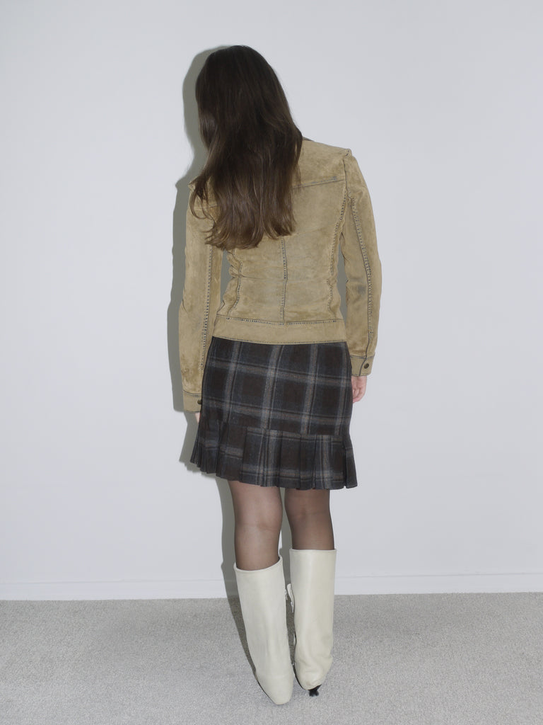 Woman wearing a structured camel suede jacket with contrast stitching, paired with a dark plaid mini skirt