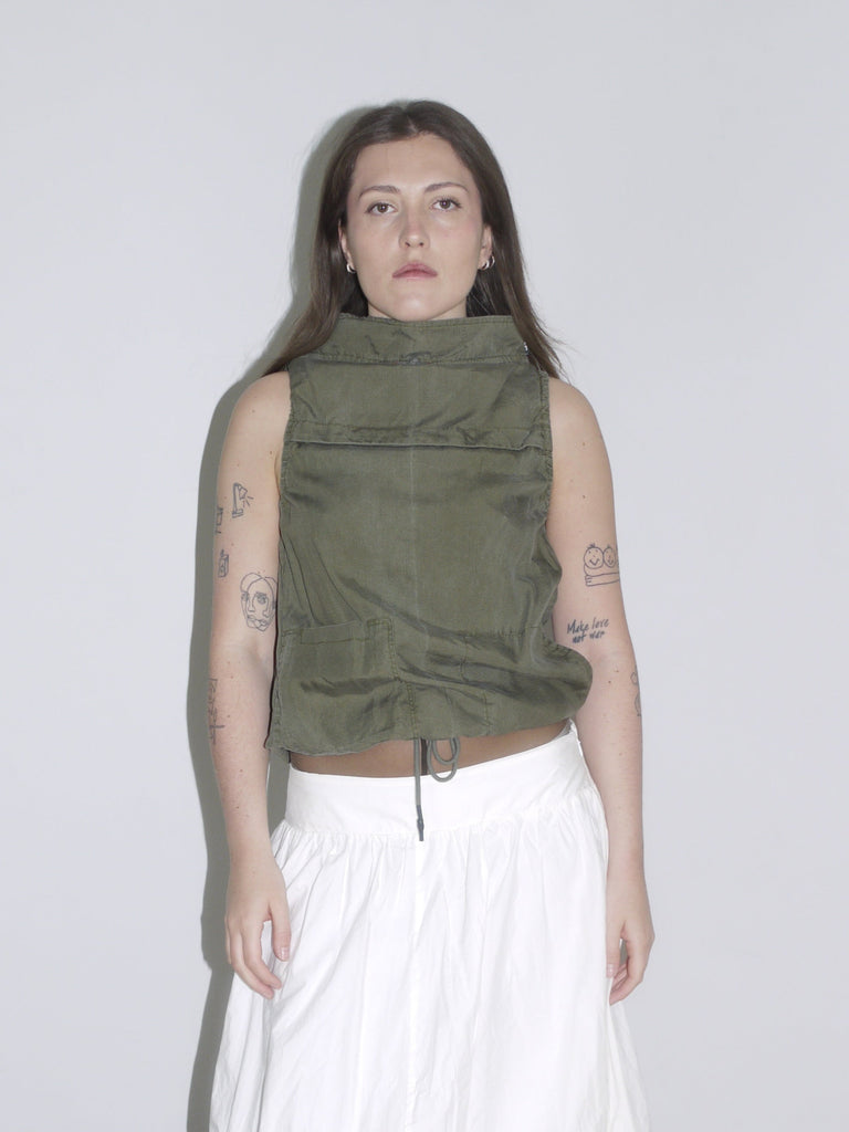 Minimalist desert-inspired outfit with an olive green sleeveless high-neck top featuring drawstring and flap pockets, styled with a voluminous white balloon skirt and cream western boots.
