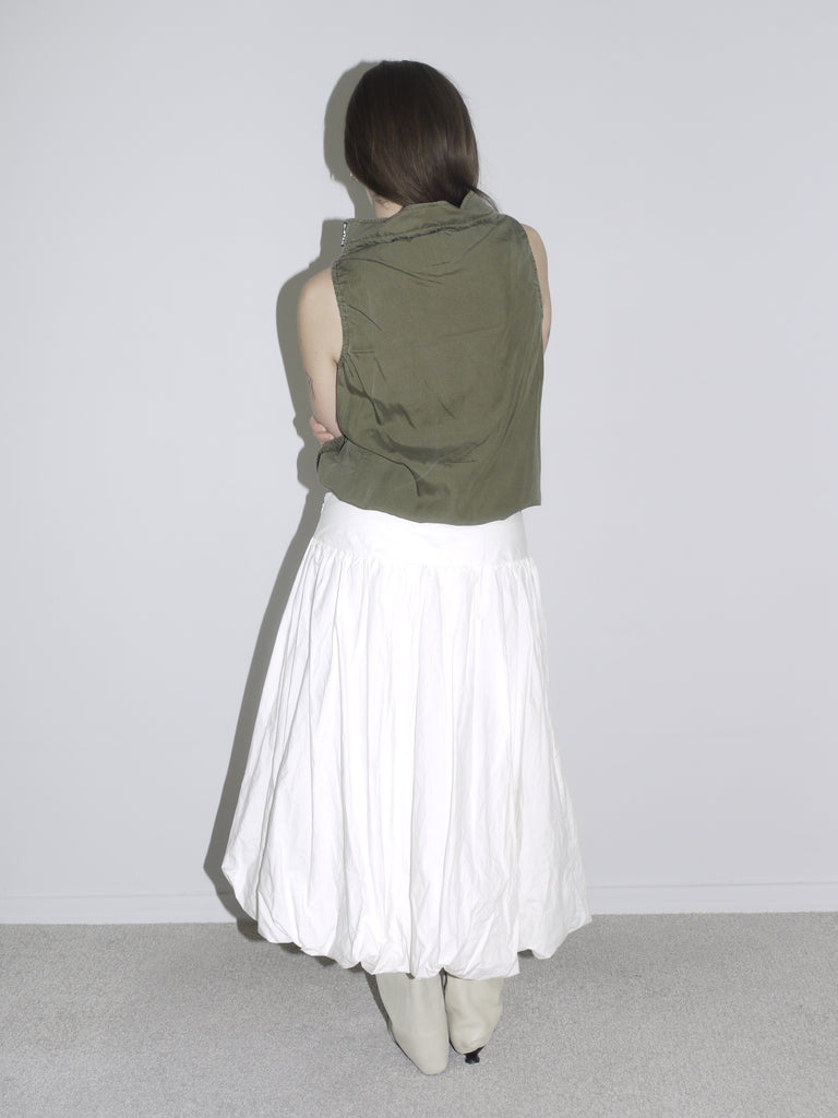 Minimalist desert-inspired outfit with an olive green sleeveless high-neck top featuring drawstring and flap pockets, styled with a voluminous white balloon skirt and cream western boots.