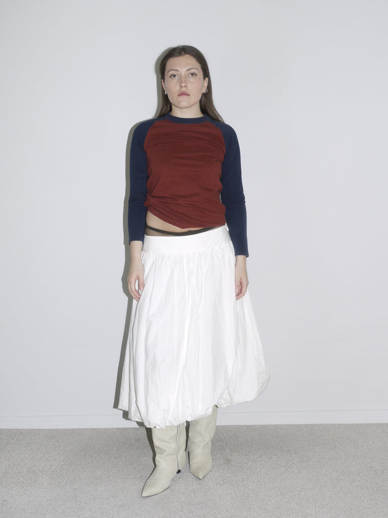 Fitted long-sleeve top with red body and navy sleeves tucked into a dramatic white skirt, giving Gimaguas meets Comme des Garçons vibes.