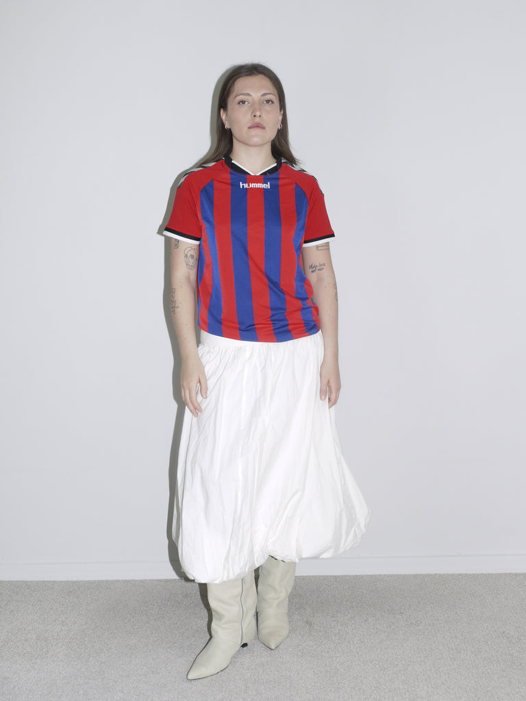 Vintage Hummel football jersey in red and blue stripes paired with a full white skirt and cream boots — sporty clash with vintage femininity.”
