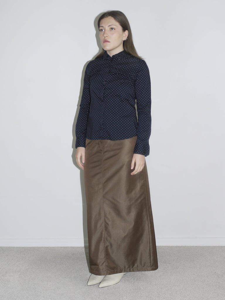 Model wearing a black sheer blouse with textured dots, styled with wide brown trousers and electric blue tights – edgy, archive-inspired look with platform heels and rectangular sunglasses.