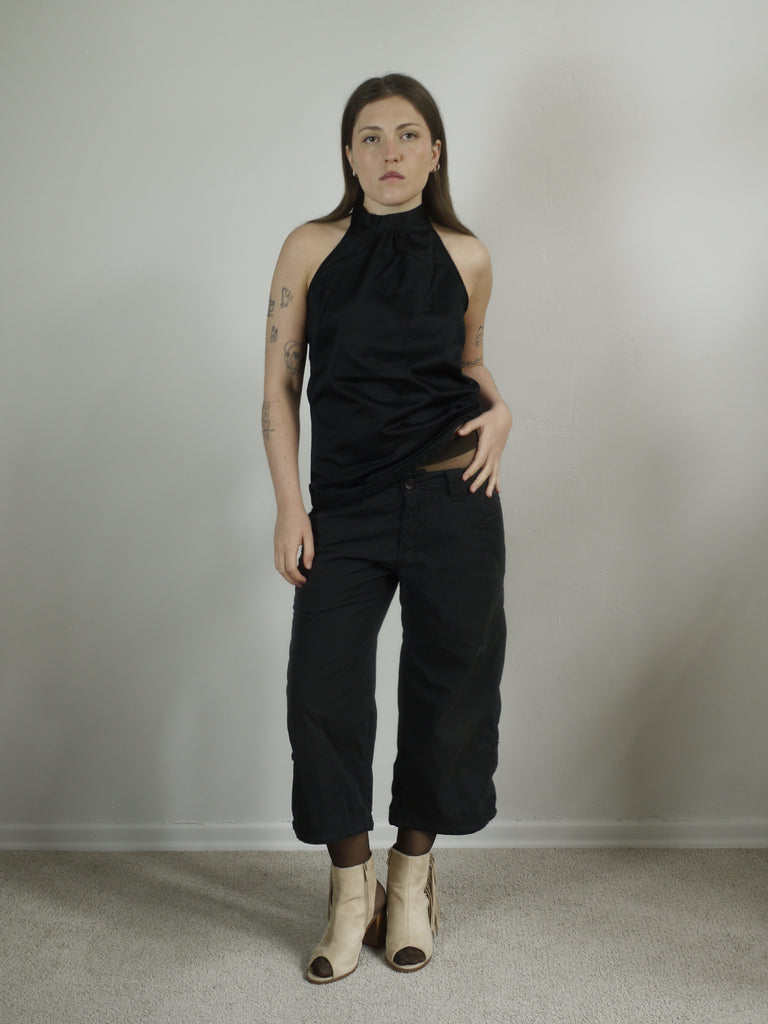 Model wearing a black halterneck top with subtle sheen, paired with cropped Nike cargo pants and beige open-toe fringe heels. A clean yet edgy Y2K silhouette — Margiela meets Nike ACG with a touch of eveningwear.