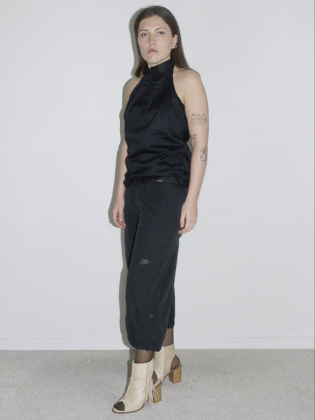 Model wearing a black halterneck top with subtle sheen, paired with cropped Nike cargo pants and beige open-toe fringe heels. A clean yet edgy Y2K silhouette — Margiela meets Nike ACG with a touch of eveningwear.