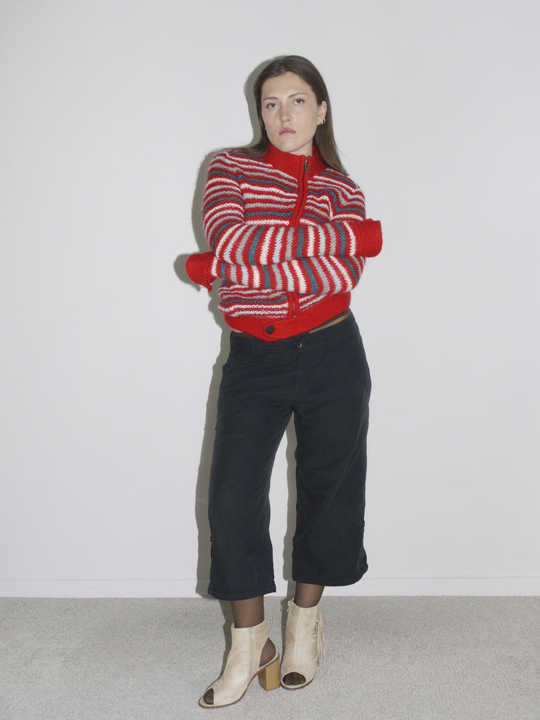Model wearing a red and white striped knit cardigan paired with low-rise, wide-leg black pants and beige open-toe boots. The look channels early 2000s streetwear with a utilitarian edge — G-Star inspired silhouette meets playful knitwear.