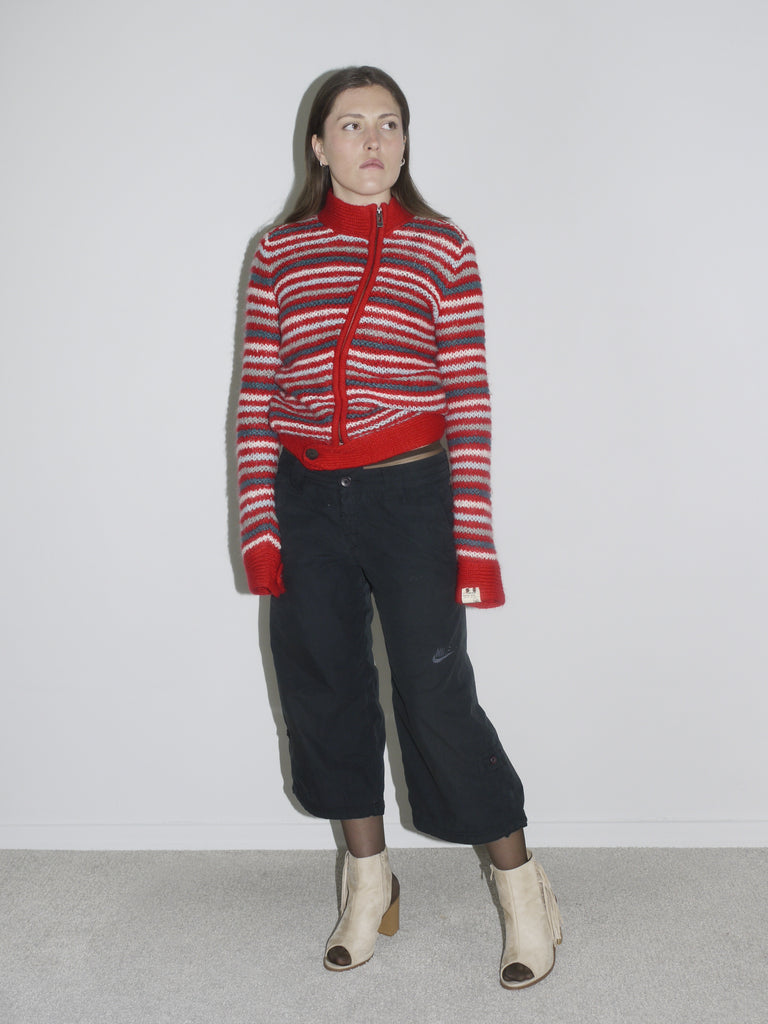 Model wearing a red and white striped knit cardigan paired with low-rise, wide-leg black pants and beige open-toe boots. The look channels early 2000s streetwear with a utilitarian edge — G-Star inspired silhouette meets playful knitwear.