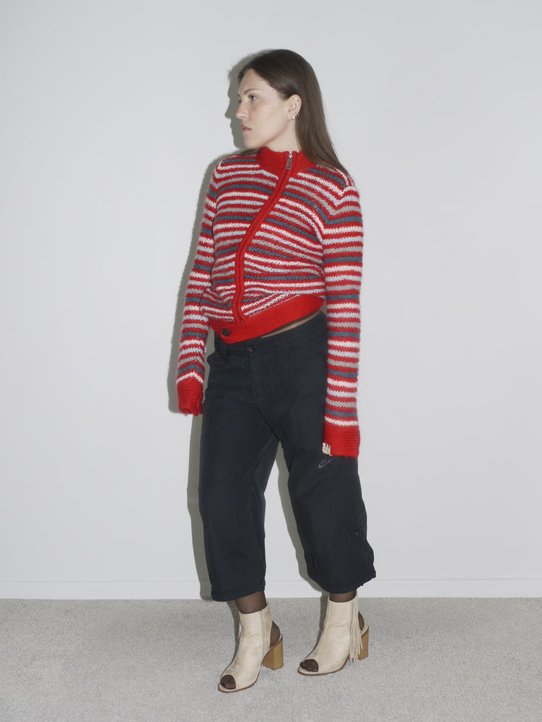 Model wearing a red and white striped knit cardigan paired with low-rise, wide-leg black pants and beige open-toe boots. The look channels early 2000s streetwear with a utilitarian edge — G-Star inspired silhouette meets playful knitwear.