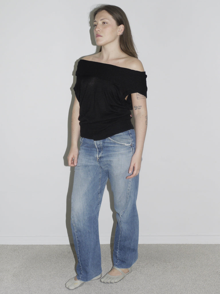 Model wearing an off-the-shoulder black knit top with relaxed fit, paired with vintage Levi’s Engineered Jeans and grey tabi-style flats. A minimal yet sensual silhouette — evoking early 2000s Helmut Lang, Ann Demeulemeester and undone Margiela femininity.