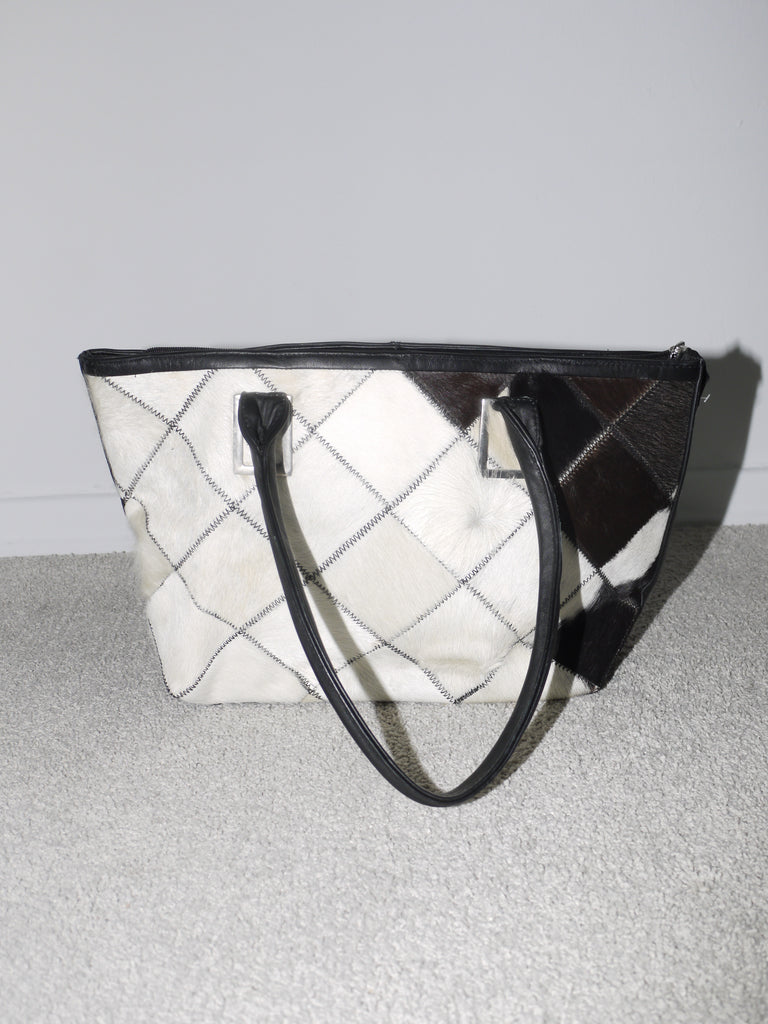Close-up of a structured black and white cowhide patchwork handbag with black leather handles. Statement vintage piece with Margiela and Diesel vibes – bold, graphic, and collectible.