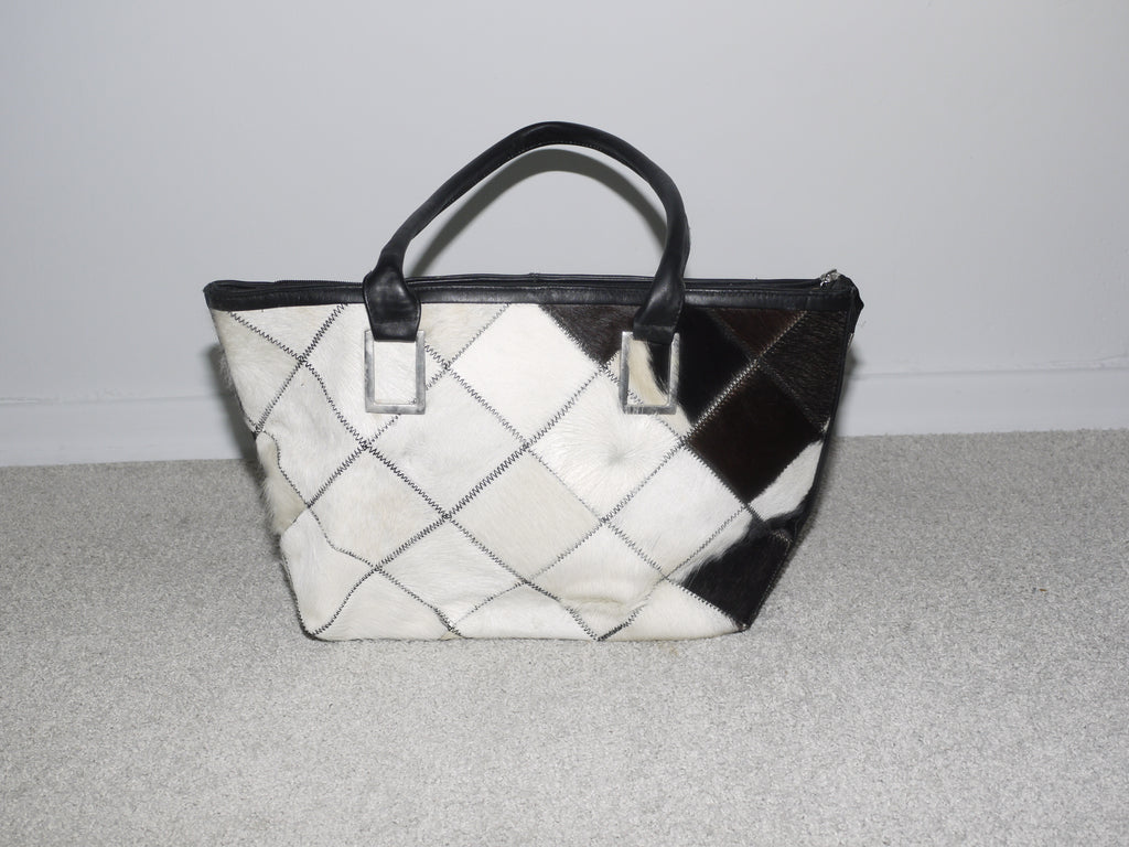 Close-up of a structured black and white cowhide patchwork handbag with black leather handles. Statement vintage piece with Margiela and Diesel vibes – bold, graphic, and collectible.