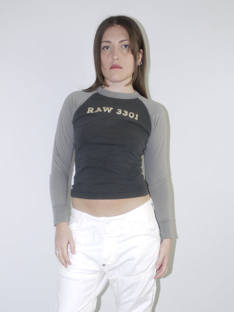 Back view of white low-rise cargo jeans with embroidered “96” detail on pocket, styled with black heeled boots and a cropped grey long sleeve top — bold Y2K revival look highlighting early 2000s denim silhouette, shot against white wall.

