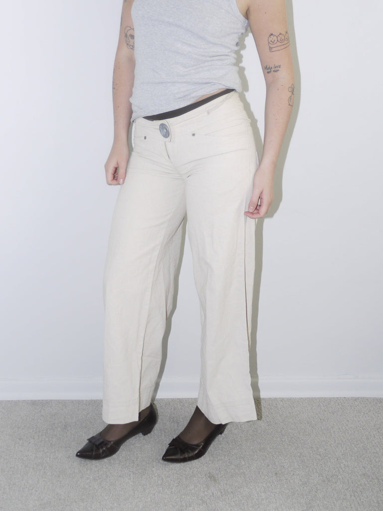 Model wearing cream wide-leg Cop Copine trousers with mid-rise waist, styled with black tights, pointed flats and a fitted grey ribbed tank top — soft minimal Y2K-inspired look with subtle Parisian edge, photographed against white background.
