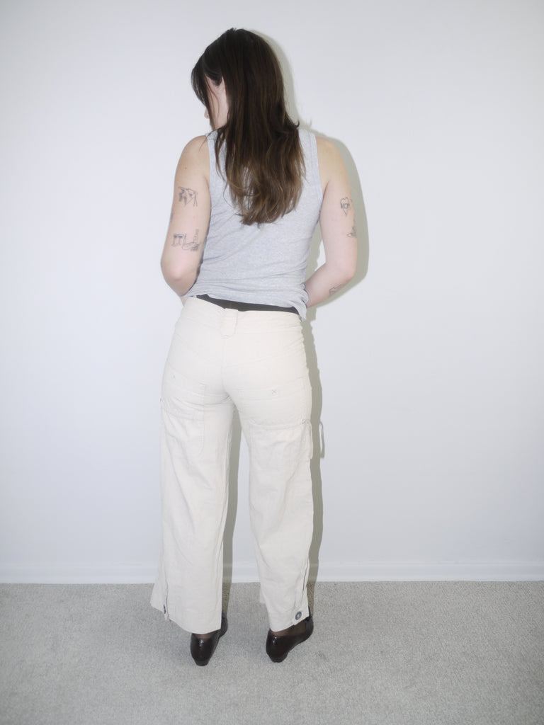 Model wearing cream wide-leg Cop Copine trousers with mid-rise waist, styled with black tights, pointed flats and a fitted grey ribbed tank top — soft minimal Y2K-inspired look with subtle Parisian edge, photographed against white background.