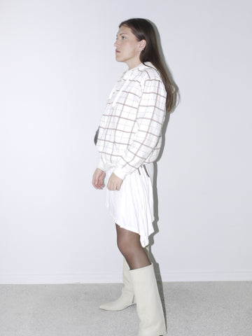 Model wearing a white grid-pattern hoodie paired with a white drawstring mini skirt, sheer black tights, and off-white pointed knee-high boots. A clean, contemporary outfit with retro sportswear vibes, styled against a plain white backdrop.