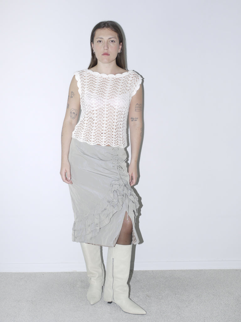 Delicate white crochet top paired with a layered, ruffled midi skirt in muted taupe, styled with white pointed knee-high boots for a soft yet structured vintage-inspired look