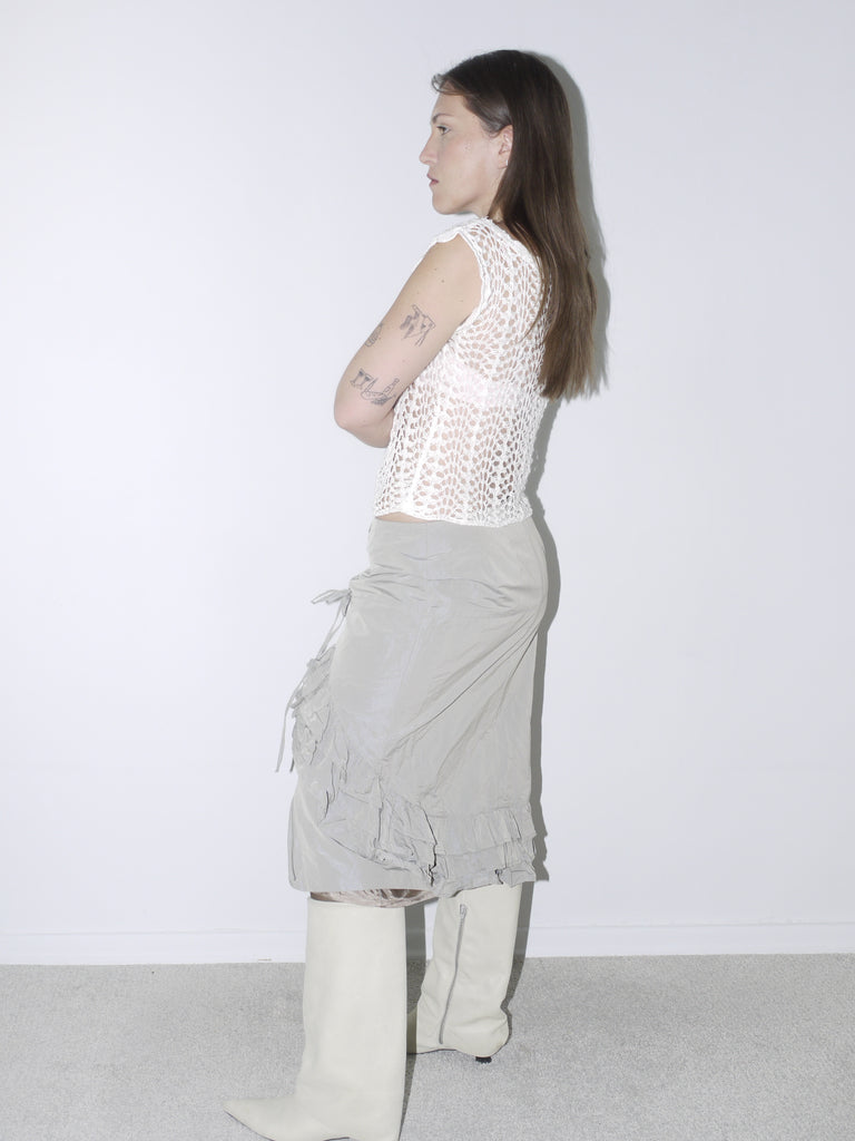 Delicate white crochet top paired with a layered, ruffled midi skirt in muted taupe, styled with white pointed knee-high boots for a soft yet structured vintage-inspired look
