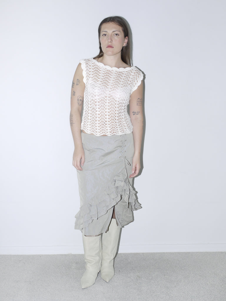 Delicate white crochet top paired with a layered, ruffled midi skirt in muted taupe, styled with white pointed knee-high boots for a soft yet structured vintage-inspired look
