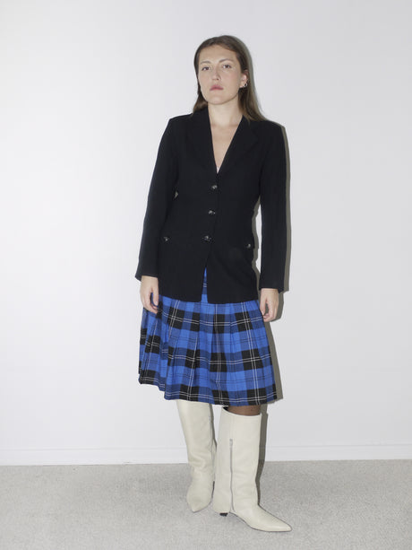 Tailored black vintage blazer with a deep V-neckline and structured silhouette, styled over a blue plaid pleated skirt and white pointed knee-high boots for a sharp, preppy-inspired look.