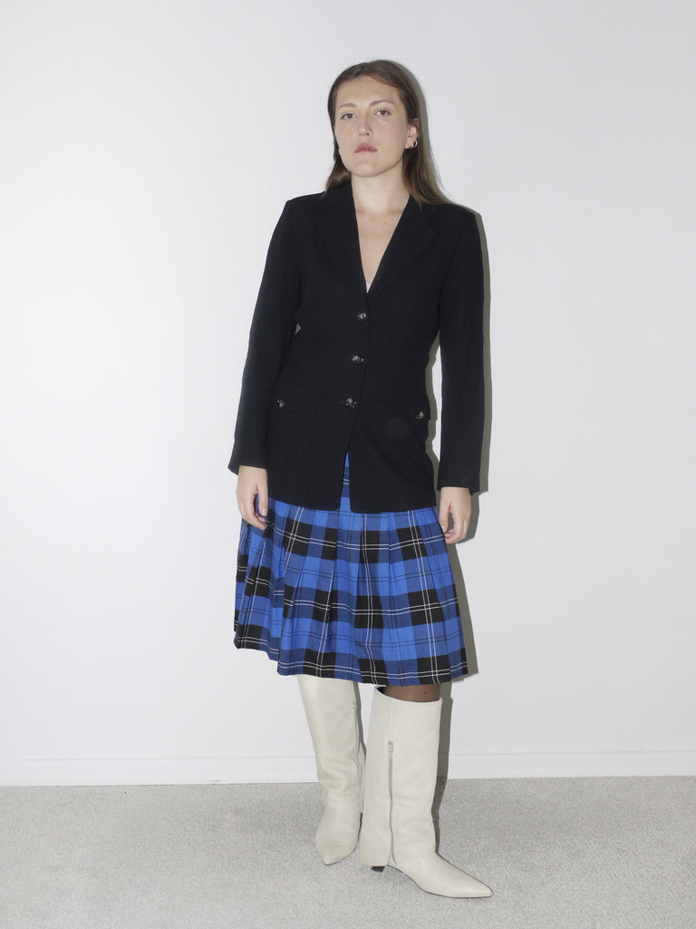 Tailored black vintage blazer with a deep V-neckline and structured silhouette, styled over a blue plaid pleated skirt and white pointed knee-high boots for a sharp, preppy-inspired look.