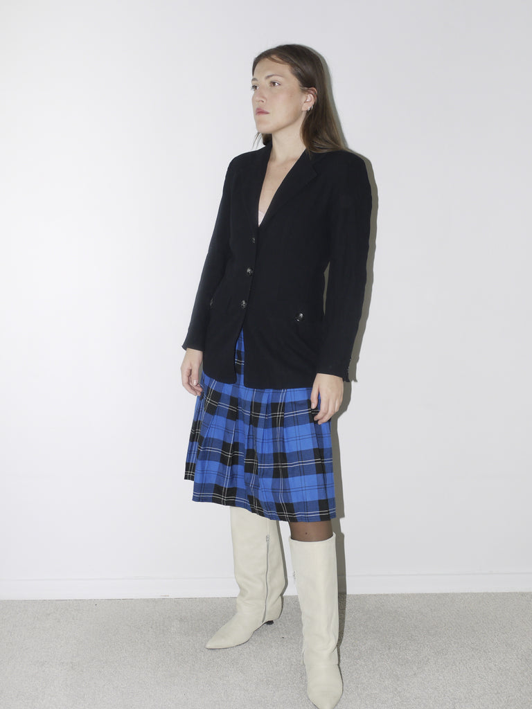 Tailored black vintage blazer with a deep V-neckline and structured silhouette, styled over a blue plaid pleated skirt and white pointed knee-high boots for a sharp, preppy-inspired look.