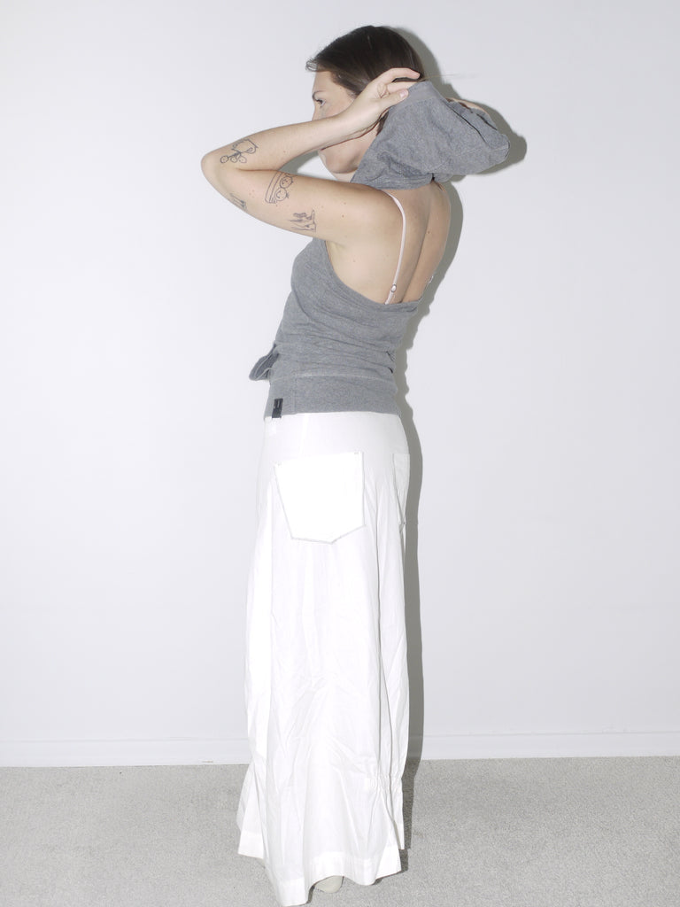 Sporty grey sleeveless hoodie with button placket, paired with a voluminous white ruched maxi skirt and white pointed knee-high boots—blending casual comfort with dramatic silhouette.